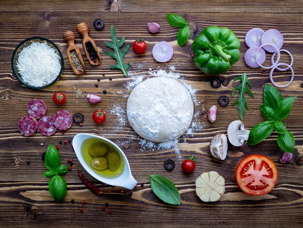 Raw dough with ingredients for homemade pizza on shabby wooden background.