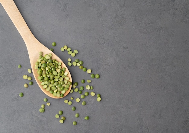 Raw dried green peas in a spoon over stone background.