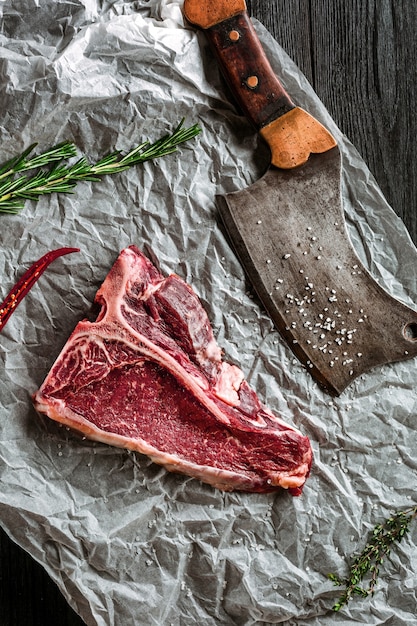 Raw dry aged tbone steaks for grill with fresh herbs and cleaver