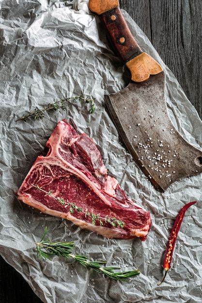 Photo raw dry aged tbone steaks for grill with fresh herbs and cleaver