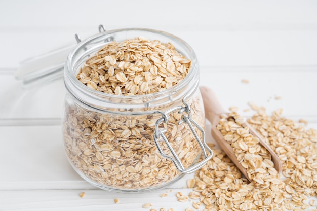 Raw dry oatmeal flakes in a glass jar on a white wooden background. Healthy food. Copy space.