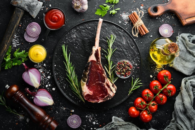 Raw dry steak on bone Tomahawk steak on a black stone background Top view Free space for your text