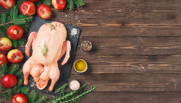 Raw duck in a baking sheet with apples and spices. ingredients on a wooden table.