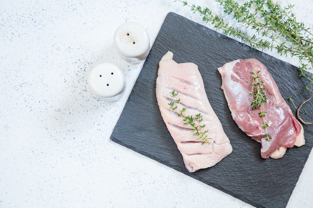 Raw duck breast on a cutting board with herbs and spices