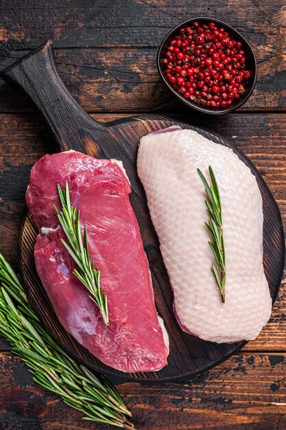 Raw Duck breast  fillet steaks on wooden cutting board with rosemary. Dark wooden background. Top View.