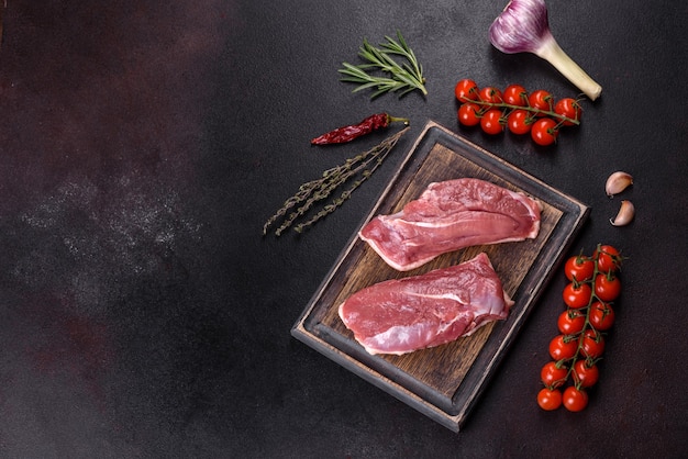 Raw duck breast with herbs and spices on a dark concrete background. Raw meat prepared for baking