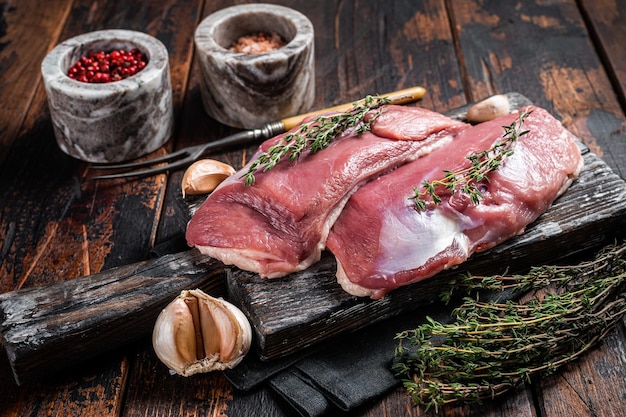 Raw Duck breasts, poultry meat steaks on wooden board ready for cooking. Wooden background. Top view.