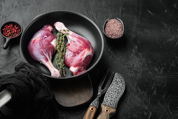 Raw duck legs. Poultry meat ready to cook set, on frying cast iron pan, on black stone table, with copyspace and space for text