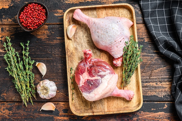 Raw Duck legs on a wooden tray.  Dark background. Top view.