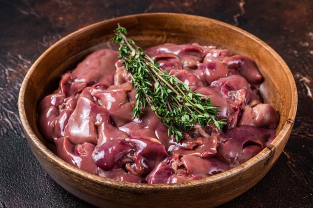 Raw duck liver offals in a wooden plate. Dark table. Top view.