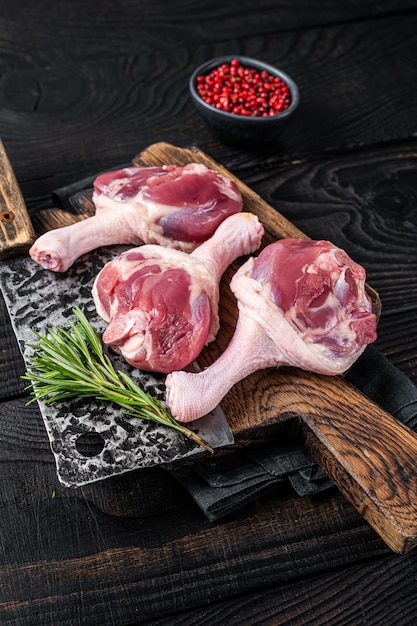 Raw Duck thighs on butcher board with meat cleaver. Black wooden background. Top view.