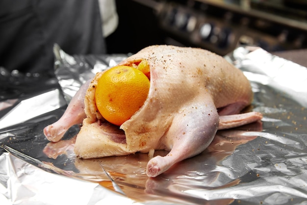 Raw duck with spices and orange on foil sheet in kitchen