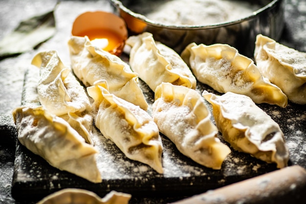 Raw dumplings gyoza on a cutting board with eggs and flour