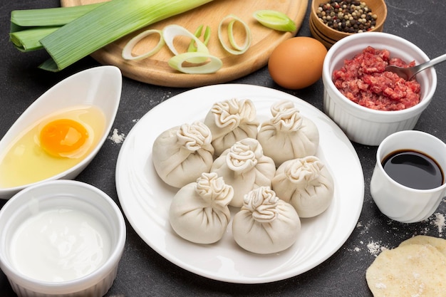 Raw dumplings on plate Ingredients for making dumplings Meat filling spices and leek Top view Black background