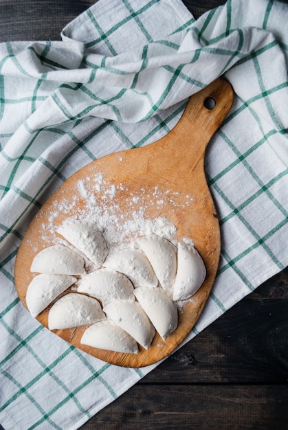 Сырые пельмени, посыпанные мукой на кухонную доску и полосатое полотенце