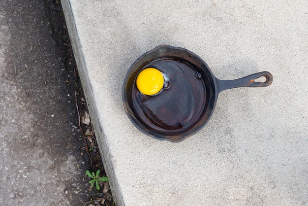Raw egg in a frying pan on the hot asphalt road fried food on the sidewalk hot weather concept summer temperature