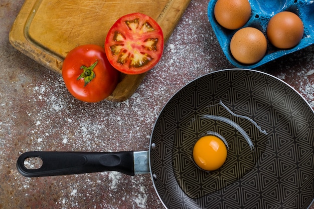 raw egg in pan or pot accompanied by tomato and fresh eggs on cutting board and flour