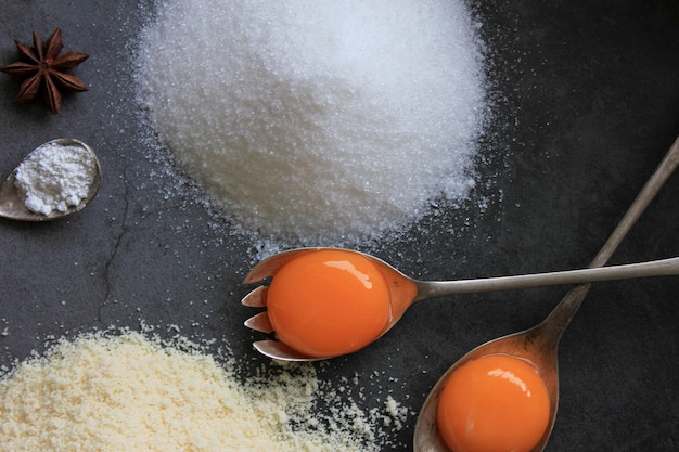 Raw egg yolk on a metal spoon Ingredients for the cake sugar almond flour cinnamon eggs Closeup