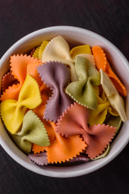 Raw farfalle pasta in different colors on a dark concrete background