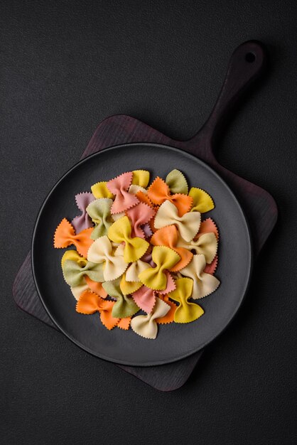 Raw farfalle pasta in different colors on a dark concrete background