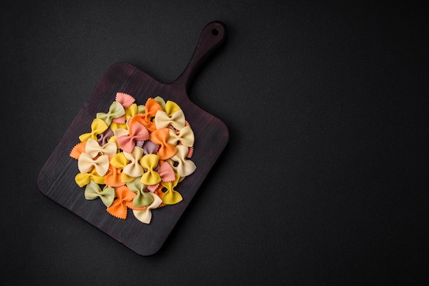 Pasta di farfalle cruda in diversi colori su uno sfondo di cemento scuro