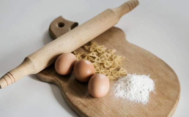 Raw farfalle pasta on wooden background with three eggs