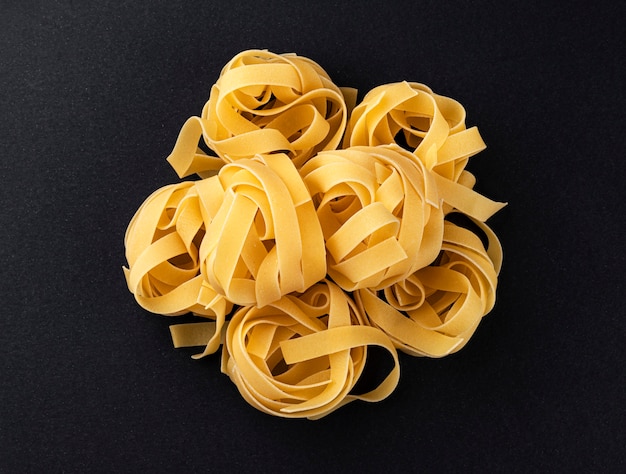 Raw fettuccine pasta isolated on black background