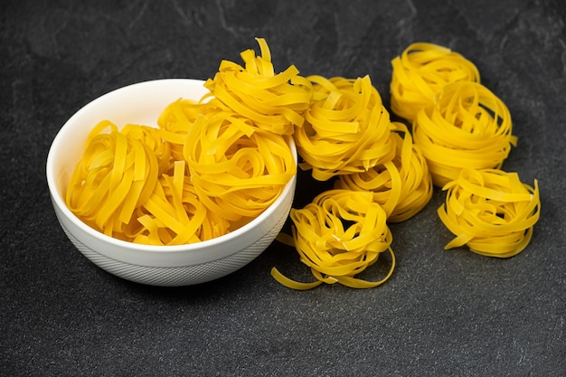 Raw fettuccine pasta in a plate isolated on dark background