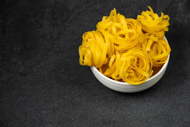 Raw fettuccine pasta in a plate isolated on dark background