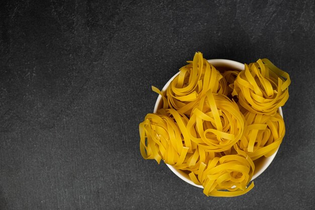 Raw fettuccine pasta in a plate isolated on dark background