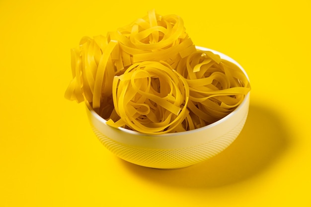 Raw fettuccine pasta in a plate isolated on yellow background