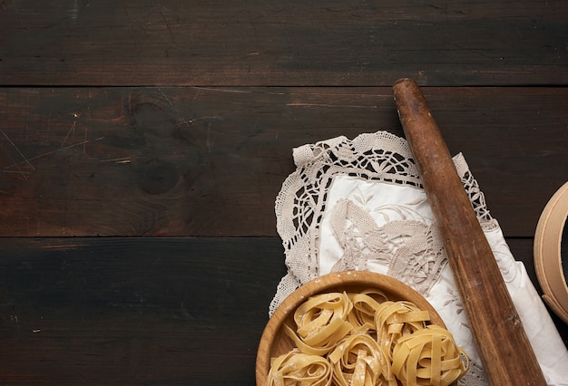 Photo raw fettuccine pasta, wooden rolling pin on a brown wooden board, top view