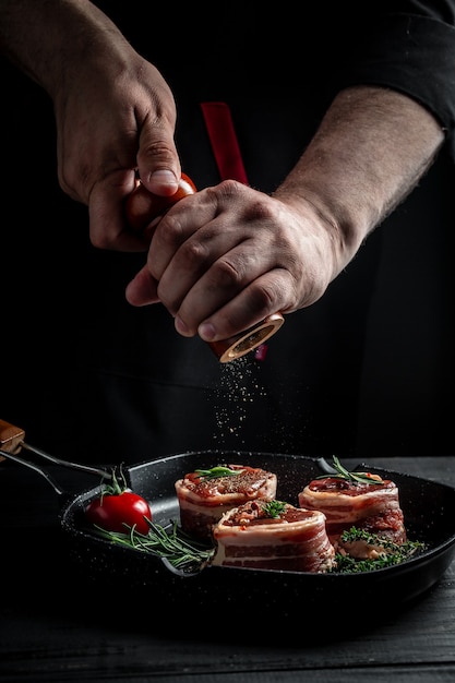 生のフィレミニョンステーキで覆われたベーコンを鍋に、肉をグリルで調理します。シェフの手でビーフステーキを調理します。メダリオンステーキ。バナー、メニューレシピ。