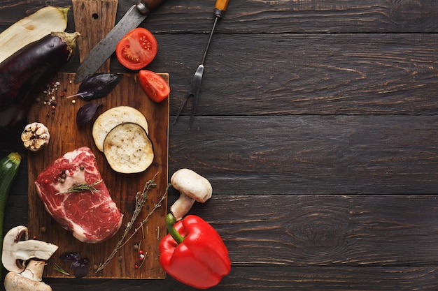 Raw filet mignon steak. Fresh beef meat on wooden board with vegetables, fork and knife. Organic ingredients for restaurant meals on kitchen table, copy space, top view