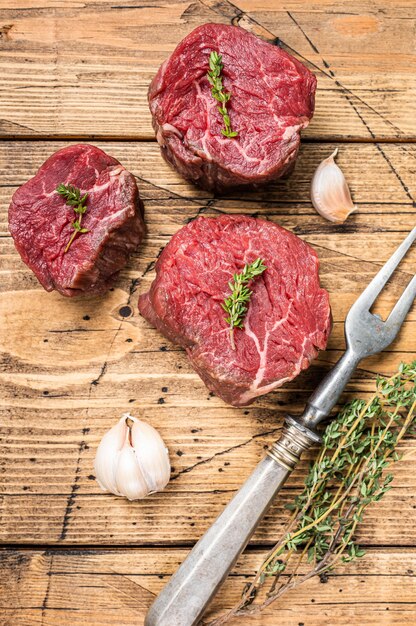 Raw Fillet mignon steaks, beef tenderloin on a wooden butcher table with meat fork. wooden background. Top view.