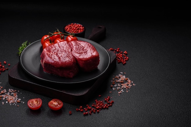 Raw fillet steak mignon beef with salt spices and herbs on a dark concrete background