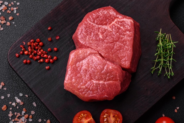 Raw fillet steak mignon beef with salt spices and herbs on a dark concrete background