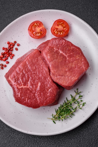 Raw fillet steak mignon beef with salt spices and herbs on a dark concrete background