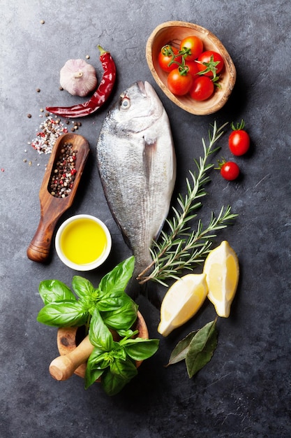 Raw fish cooking and ingredients dorado lemon herbs and spices top view on stone table