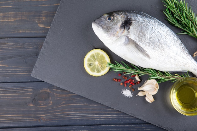 Raw fish dorado cooking and ingredients.  Dorado, lemon, tomato, herbs and spices. Top view on wood table