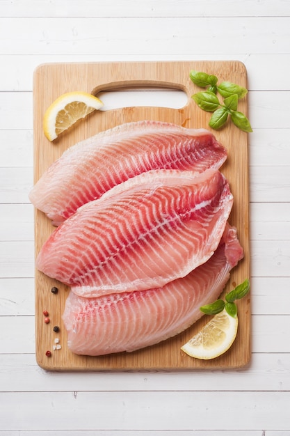 Filetto di pesce crudo di tilapia su un tagliere con limone e spezie