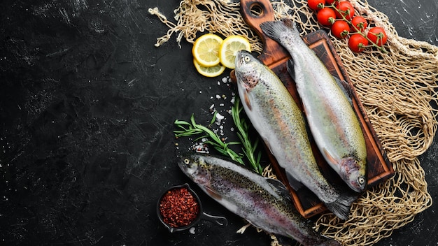 Raw fish trout with vegetables on a black stone background Top view Free space for your text