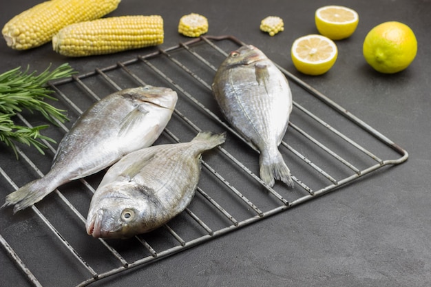 Raw fish with corn and lemon on grill. Sprigs of rosemary.