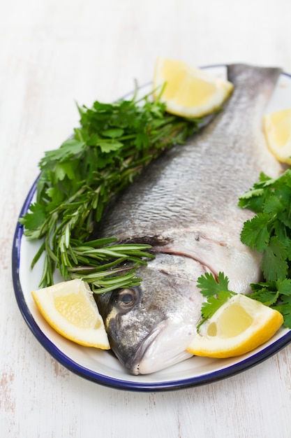 Raw fish with herbs and lemon on dish on wooden surface