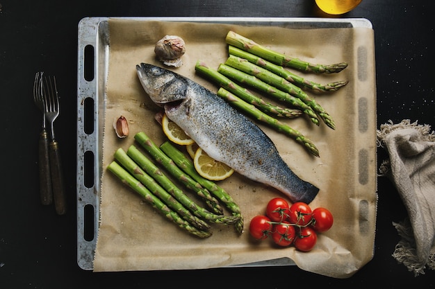 Raw fish with spices and vegetables asparagarus on baking sheet ready to be cooked