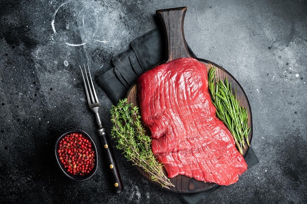 Raw flank beef steak uncooked meat with herbs Black background Top view