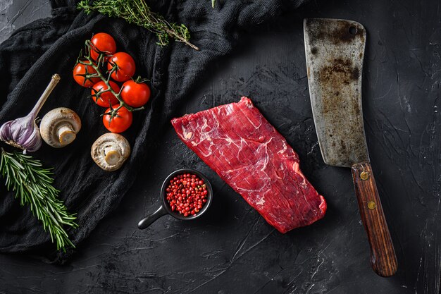 Cruda, lembo o sul fianco, nota anche bistecca di bavette vicino al coltello da macellaio con pepe rosa e rosmarino. sfondo nero. vista dall'alto.