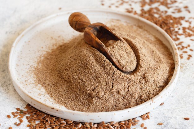 Raw Flax seeds flour in a ceramic plate with a spoon close up