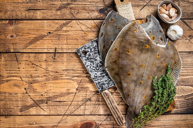 Raw flounder flatfish on butcher board with cleaver. wooden background. top view. copy space.