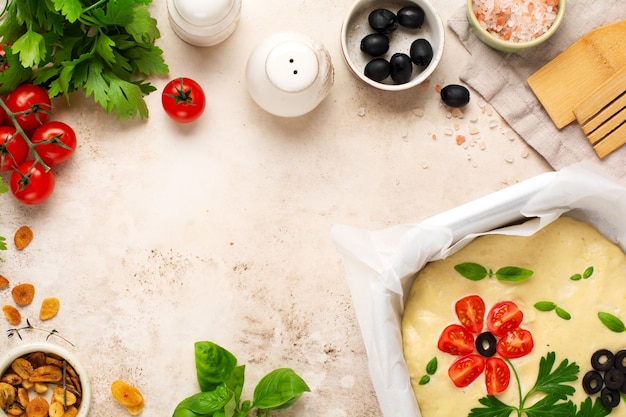 Raw focaccia creatively decorated with vegetables on parchment paper. Homemade flower focaccia. Sourdough dough. Decorated Italian bread. Top view